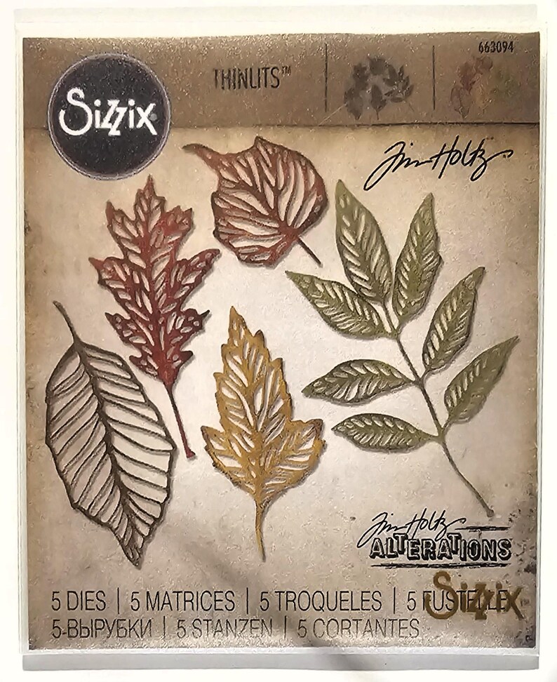 Op de afbeelding: Een pakket Sizzix Thinlits stansmessen met zes verschillende bladvormen in bruin, rood en goud. Het pakket bevat de tekst "Sizzix", "Thinlits", "Jim Holtz" en "Alterations". Het pakket bevat ook de tekst "5 DIES | 5 MATRICES | 5 TROQUELES | 5 FUSTELE | 5-ВЫРУБКИ | 5 STANZEN | 5 CORTANTES".
