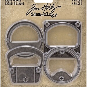 May include: Four metal gauge frames in a clear plastic packaging. The frames are in different shapes, including round, oval, and rectangular. The packaging has the text "GAUGE FRAMES" and "CADRES DE JAUGE" printed on it. The packaging also has the text "Jim Holtz idea-ology" printed on it. The packaging has the text "4 PIECES" and "4 PIÈCES" printed on it.