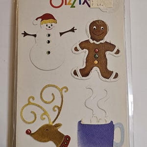 May include: A Sizzix Snow Set die-cut package featuring a snowman, gingerbread man, reindeer, and a cocoa mug. The package includes the text "cocoa" and "Sizzlits". The package also includes the text "Image Shown 100%, Embellished".