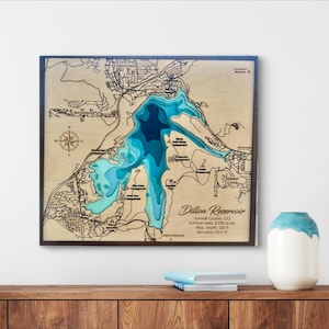 Puede incluir: Un mapa de madera del embalse de Dillon, condado de Summit, CO, con un marco oscuro. El mapa muestra los contornos del lago en tonos de azul, con texto que indica la superficie, la profundidad y la elevación. Una rosa de los vientos está arriba a la izquierda.