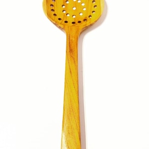 May include: A wooden slotted spoon with a long handle. The spoon is made of light brown wood and has a round, perforated head.