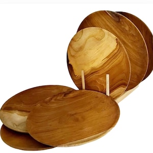 May include: Set of six wooden plates, made from natural teak wood. The plates are round and have a light brown colour. The plates are stacked on top of each other.