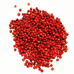 May include: A close-up image of a pile of red peppercorns. The peppercorns are small and round, and they are all a vibrant red colour.