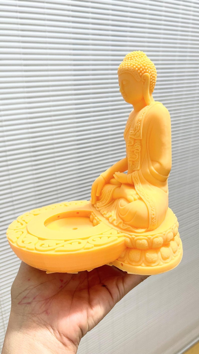 K&ouml;nnte beinhalten: Eine gelbe Buddha-Statue in sitzender Meditationshaltung. Die Statue steht auf einem runden Sockel mit dekorativem Rand. Der Kopf des Buddha hat ein strukturiertes Muster, und die Figur h&auml;lt die H&auml;nde in einer meditativen Geste.