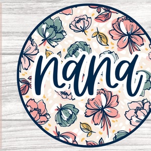 May include: A round sticker with a floral pattern in shades of pink, green, and yellow. The word "nana" is written in a navy blue cursive font on top of the floral pattern.