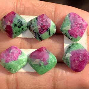 Peut inclure: Six pierres précieuses facettées de forme carrée. Les gemmes présentent une combinaison de couleurs vives, rose foncé et vert. Les pierres sont présentées sur une surface blanche.