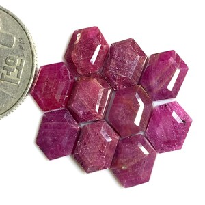 May include: A collection of ten faceted ruby gemstones in a hexagonal shape. The rubies are a deep red color with a slight pink hue.