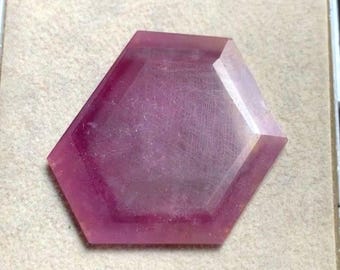 Op de afbeelding: Een gefacetteerde, zeshoekige edelsteen met een dieproze tint. De edelsteen is geplaatst tegen een neutrale achtergrond, waardoor de gepolijste oppervlakken en geometrische vorm worden benadrukt. De kleur van de edelsteen varieert van lichtroze tot een donkerder, meer verzadigd roze.