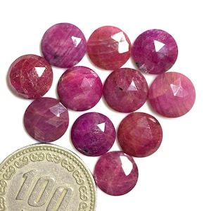Puede incluir: Una colección de diez piedras preciosas de rubí facetadas, cada una con un tono rosado y un matiz ligeramente diferente. Las piedras preciosas están dispuestas en un grupo suelto, con algunas superposiciones.