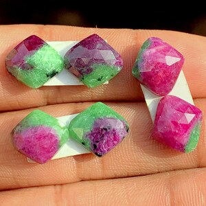 Pode incluir: Seis pedras preciosas facetadas em forma quadrada. Cada gema apresenta um centro rosa vibrante e roxo escuro, rodeado por uma borda verde. As gemas são exibidas em um fundo branco.