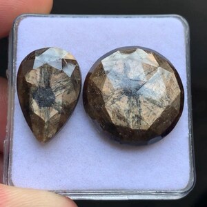 Peut inclure: Deux pierres précieuses facettées avec un motif en forme d'étoile marron et noir. Une pierre est en forme de poire et l'autre est ronde. Les deux pierres sont présentées dans un boîtier en plastique transparent avec un insert en mousse blanche.