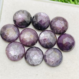 May include: A collection of ten faceted, round gemstones. The gems are a deep purple color with a polished, reflective surface. The gemstones are arranged closely together, filling the frame.