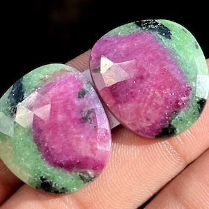 Peut inclure: Deux pierres précieuses facettées aux couleurs vives. Les pierres présentent une zone centrale rose foncé, entourée d'une bande verte et rehaussée d'inclusions noires. Les gemmes sont polies et ont une surface lisse et réfléchissante.