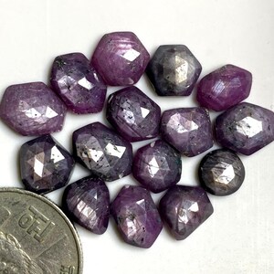 Può includere: Una collezione di 14 pietre preziose viola sfaccettate, ognuna con una forma e una dimensione uniche. Le pietre preziose hanno una tonalità viola profonda con un leggero luccichio.