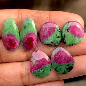 Puede incluir: Seis gemas facetadas con una mezcla de colores. Las gemas tienen un vibrante centro rojo, rodeado de inclusiones verdes y negras. Las formas varían de ovaladas a redondeadas, mostrando la belleza natural de las piedras.