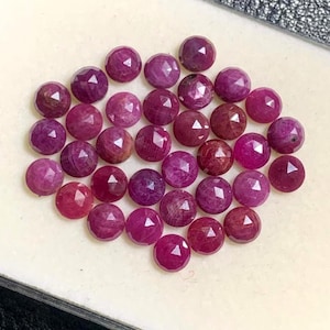 May include: A collection of faceted, round gemstones in varying shades of red and purple. The gemstones are arranged closely together, showcasing their polished surfaces and geometric cuts. The overall effect is a display of vibrant, natural gemstones.
