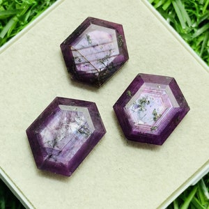 May include: Three purple faceted gemstones with a hexagonal shape. The gemstones have a sparkly, iridescent appearance.