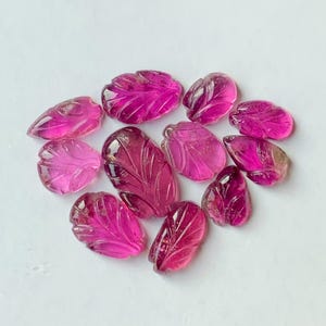 Op de afbeelding: Een verzameling gesneden roze edelstenen in de vorm van bladeren. De edelstenen variëren in grootte en vorm, met ingewikkelde details van aderen en texturen. De kleur varieert van licht- tot dieproze, met een doorschijnende kwaliteit.