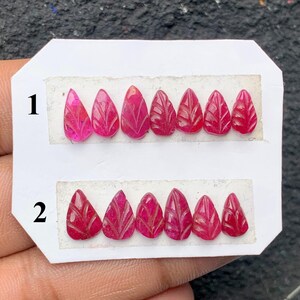 Peut inclure: Une collection de pierres précieuses taillées en forme de goutte d'eau, de différentes nuances de rose et de rouge, disposées sur une carte blanche. Les pierres précieuses sont gravées de motifs en forme de feuilles. La carte est numérotée 1 et 2.