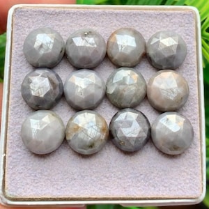 May include: A collection of twelve round, faceted gray gemstones arranged in a three-by-four grid. Each stone features a polished, multi-faceted surface that reflects light, displaying subtle variations in tone from light to medium gray.