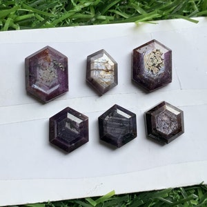 Peut inclure: Six pierres précieuses de forme hexagonale avec un schéma de couleurs violet et gris. Les pierres précieuses sont disposées en deux rangées de trois sur une surface blanche.