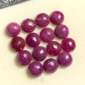 Op de afbeelding: Een verzameling gefacetteerde, ronde robijn edelstenen. De robijnen hebben een dieprode tot roze kleur en een gepolijst, reflecterend oppervlak. De edelstenen zijn dicht bij elkaar geplaatst, wat hun slijpsel en kleur laat zien.