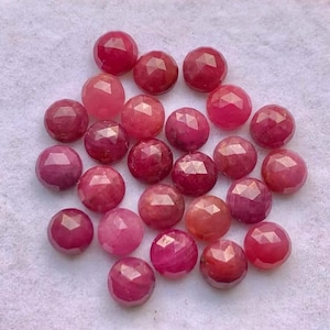 Può includere: Una collezione di pietre preziose rotonde e sfaccettate nei toni del rosso e del rosa. Le pietre preziose hanno una superficie lucida e riflettente e sono sparse su uno sfondo bianco. Le gemme variano dal rosa chiaro al rosso intenso.