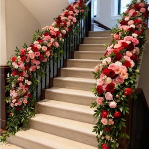 May include: A staircase adorned with vibrant floral arrangements. Lush garlands of red and pink roses, interspersed with greenery, cascade along the banisters. The steps are a neutral beige, creating a striking contrast with the colorful flowers.