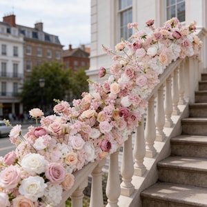 Może przedstawiać: Balustrada schodów ozdobiona kompozycją kwiatową z różowych i białych kwiatów. Kwiaty kaskadowo opadają na białą balustradę, tworząc kwiatową ekspozycję. Schody są kamienne.
