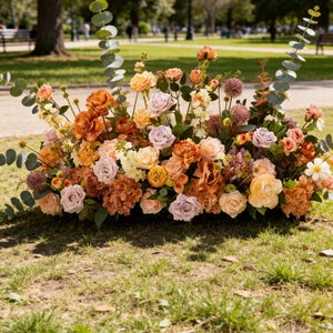 May include: A large floral arrangement featuring a mix of orange, peach, lavender, and cream-coloured roses, hydrangeas, and spherical thistle flowers, accented with tall eucalyptus stems and green foliage, displayed in a low, wide base.