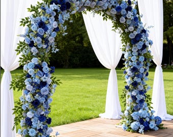 Puede incluir: Un arco floral adornado con una variedad de flores azules, incluyendo rosas y hortensias, crea un punto focal impresionante. Telas blancas drapeadas cuelgan detrás del arco, sobre una plataforma de madera con un fondo de césped verde.