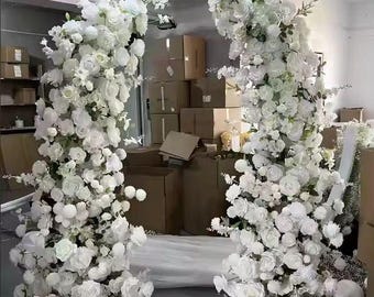 May include: White floral archway made of artificial flowers, perfect for a wedding ceremony or special event. The arch is made of white roses, hydrangeas, and other flowers.