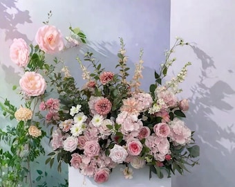 May include: A vibrant floral display featuring a mix of pink and white flowers, such as roses, peonies, and carnations, with green foliage. The arrangement is cascading, creating a full and lively look. The flowers are arranged in a cascading style, creating a full and vibrant display.