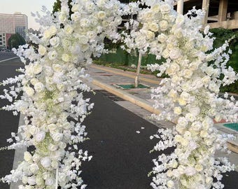 May include: A white floral archway made of artificial flowers, perfect for a wedding or special event. The archway is made of white roses, hydrangeas, and other flowers.