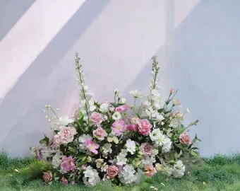 May include: A vibrant floral display with pink, white, and cream flowers, including roses. The arrangement is set against a backdrop of green foliage, creating a soft, romantic aesthetic. The flowers are artfully arranged, showcasing a variety of blooms.