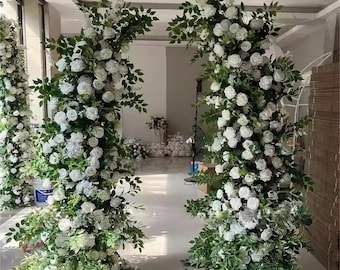 May include: Two white flower arrangements with green leaves, each standing tall and creating a decorative archway. The flowers are arranged in a cascading style, creating a romantic and elegant look.