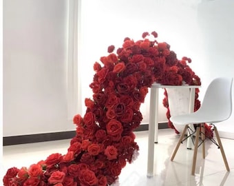 May include: A large floral arrangement made of red roses and carnations, cascading down a white table and onto the floor. The arrangement is perfect for a wedding or other special event.
