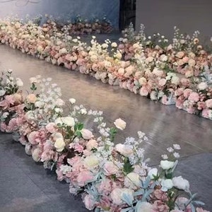 May include: A floral arrangement featuring rows of pink and white flowers, creating a pathway effect. The flowers are arranged in rectangular containers, with a variety of blooms and greenery. The overall color palette is soft and romantic, suitable for weddings or events.
