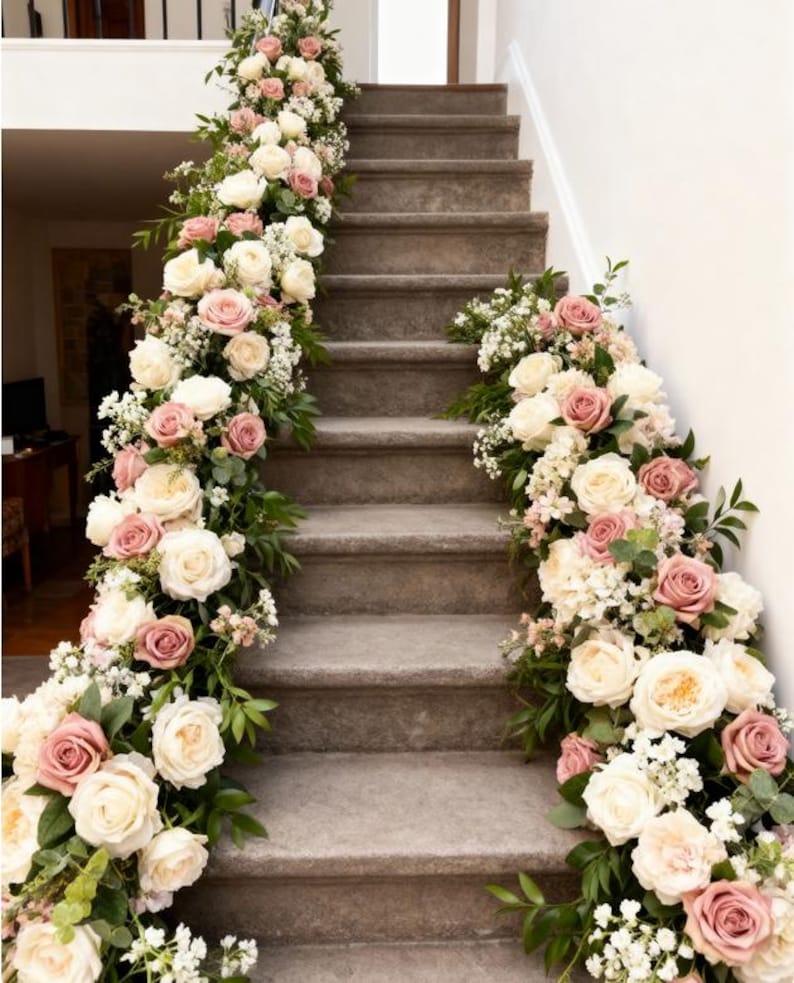 May include: A staircase decorated with floral arrangements. The steps are adorned with garlands of white and dusty rose roses, accented by greenery and small white flowers. The arrangement cascades down the side of the stairs.