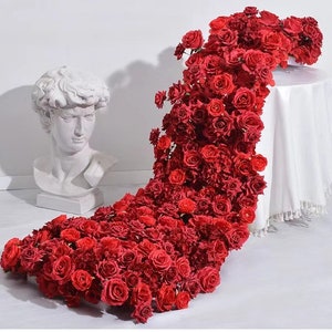 Puede incluir: Una cascada de rosas rojas artificiales, que caen desde un pedestal blanco, creando una exhibición floral dramática y romántica.