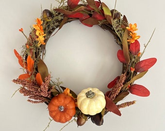 May include: A fall-themed wreath with a brown twig base, decorated with orange and white pumpkins, red and orange leaves, and small brown acorns.