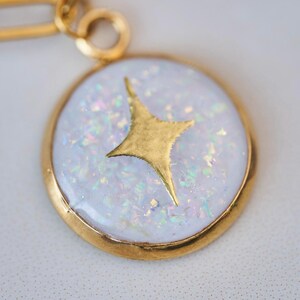 May include: A gold chain necklace with a round pendant featuring a white opal-like stone with a gold star design.
