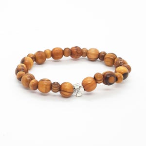 May include: A brown wooden beaded bracelet with a silver cross charm. The beads are made of olive wood and have a natural wood grain.