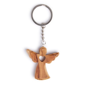 Puede incluir: Un llavero de madera con forma de ángel con un corazón recortado. El ángel está hecho de madera de olivo y tiene un acabado de madera natural. El llavero está unido a un anillo de metal plateado.
