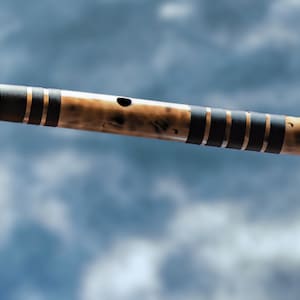 Op de afbeelding: Een bruine bamboefluit met zwarte en gouden accenten. De fluit is gemaakt van natuurlijke bamboe en heeft een traditioneel ontwerp.