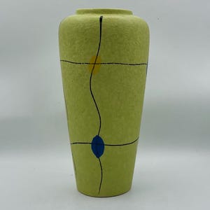 Könnte beinhalten: Eine grüne Keramikvase mit strukturierter Oberfläche und schwarzen, blauen und gelben geometrischen Mustern.