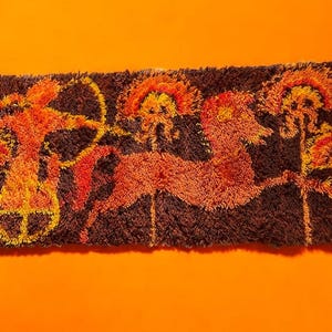 May include: A rectangular, brown, tufted rug with an orange background. The rug features a stylized design of a chariot, a running animal, and stylized trees in shades of orange and yellow.
