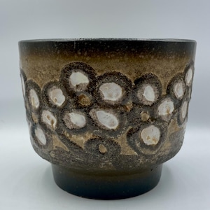 Op de afbeelding: Een keramische plantenbak met een donkerbruine basis en een cilindrisch lichaam. Het lichaam heeft een patroon van witte en bruine cirkelvormige vormen. De bovenrand is een donkerdere bruintint, waardoor een gradiënteffect ontstaat.