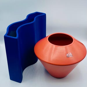 May include: Two ceramic vases, one blue and one orange. The blue vase is wavy and the orange vase is round with a wide opening.