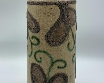 Könnte beinhalten: Eine zylindrische Keramikvase mit beigefarbener Grundfarbe. Die Vase ist mit braunen blattartigen Formen und grünen, wirbelnden Ranken verziert. Der Rand und der Boden haben einen strukturierten, dunkelbraunen Rand. Die Vase hat einen leicht verjüngten Hals.